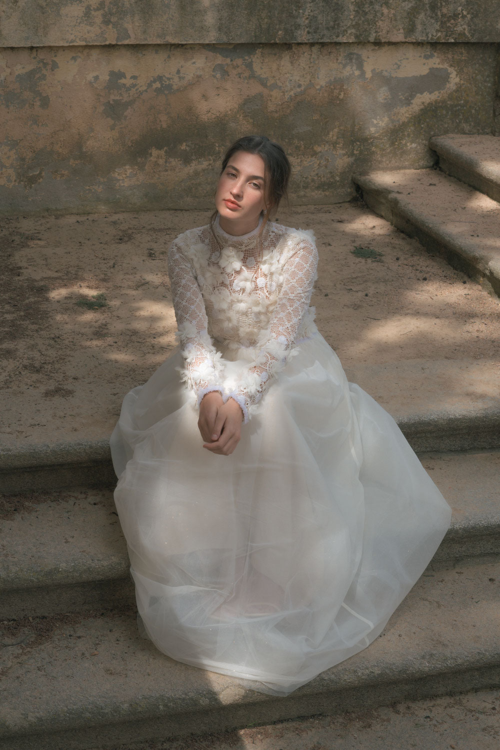 Mujer sentada en escalera con vestido Fiora de Naas atelier Vestido Fiora de Naas Atelier  confeccionado en guipur floral bordado con manga larga.